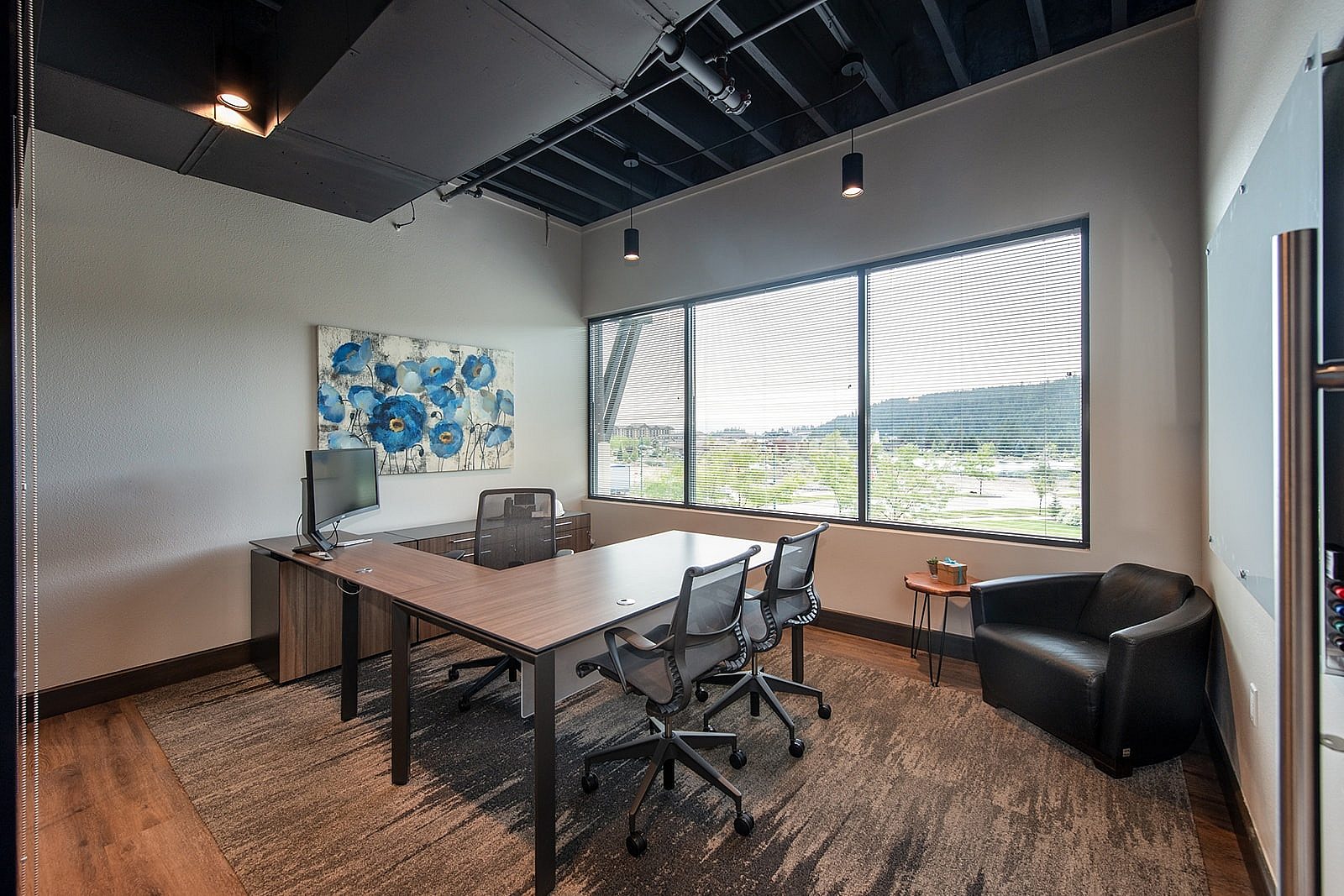 Small work station wth a view, windows, with desk and chairs and uphostered chair in corner