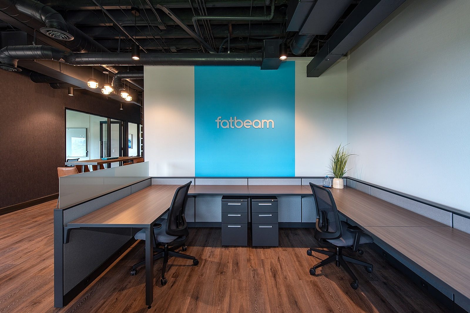 Inside the reception area, work desks, task chairs, filing cabinets and Fatbeam logo in white on large blue stripe on wall in the background